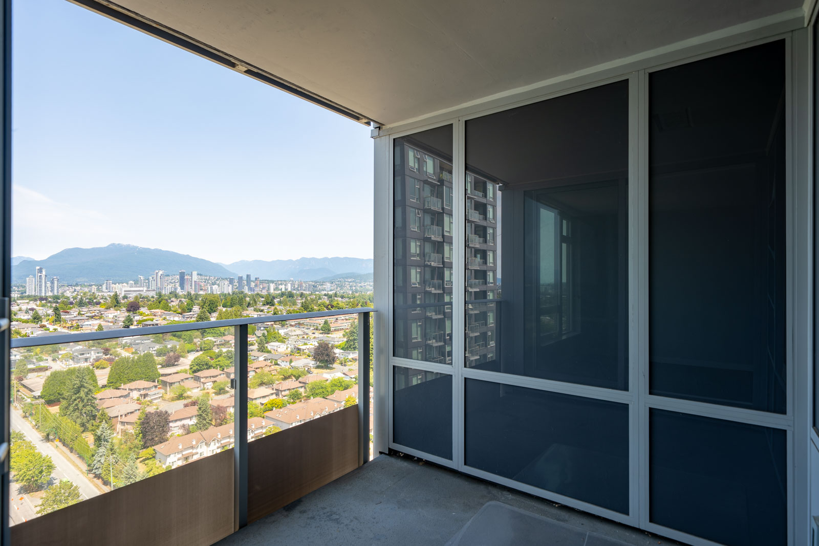 High-rise balcony with glass railing overlooking Vancouver’s skyline, greenery, distant mountains, and Boundary Rd below.