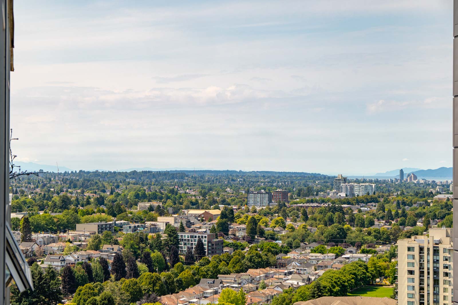 Residential buildings and green trees line Vancouver's Boundary Rd, with hills in the distance under a partly cloudy sky.