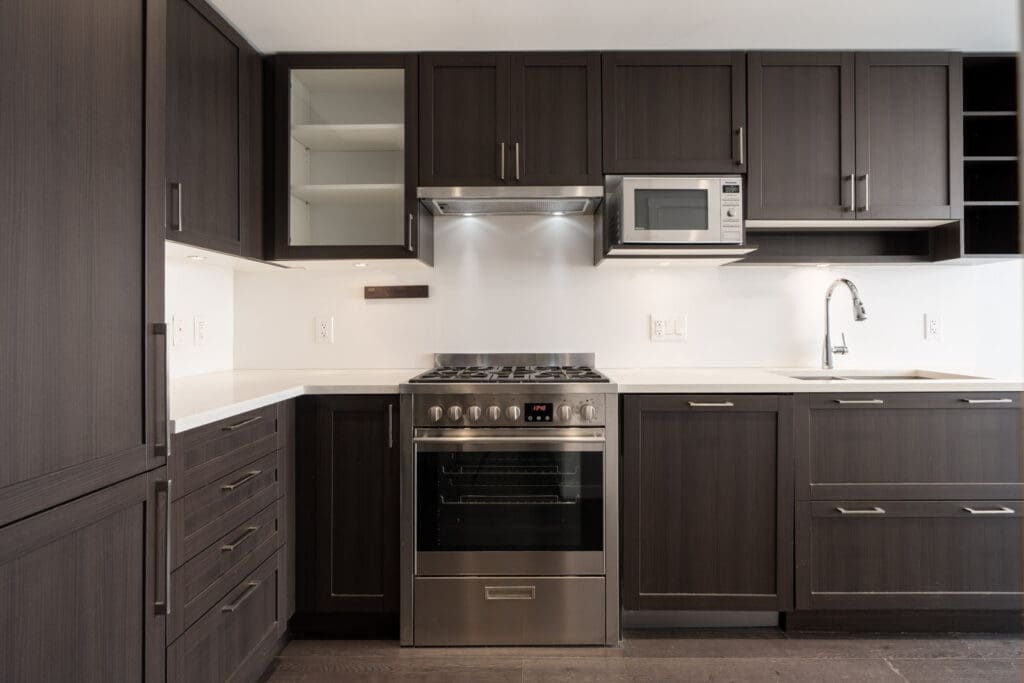 Modern kitchen on Boundary Rd, Vancouver with dark cabinets, stainless stove, built-in microwave, white counters, and under-mount sink.