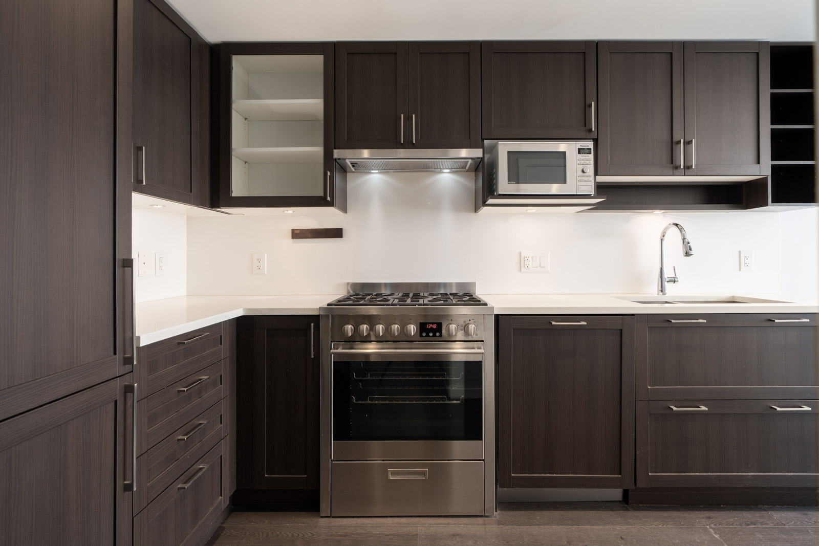 Modern Vancouver kitchen with dark wood cabinets, stainless steel appliances, open cabinet with empty shelves, white counters.