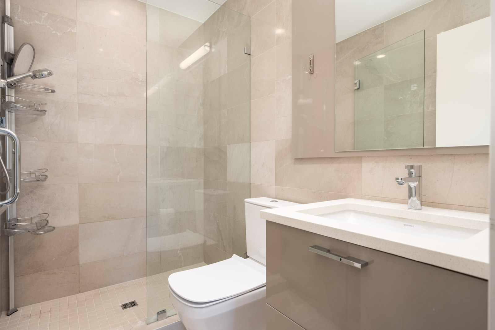 Modern bathroom with beige tiles, a glass-enclosed shower, white toilet, and a vanity with a rectangular sink and large mirror.