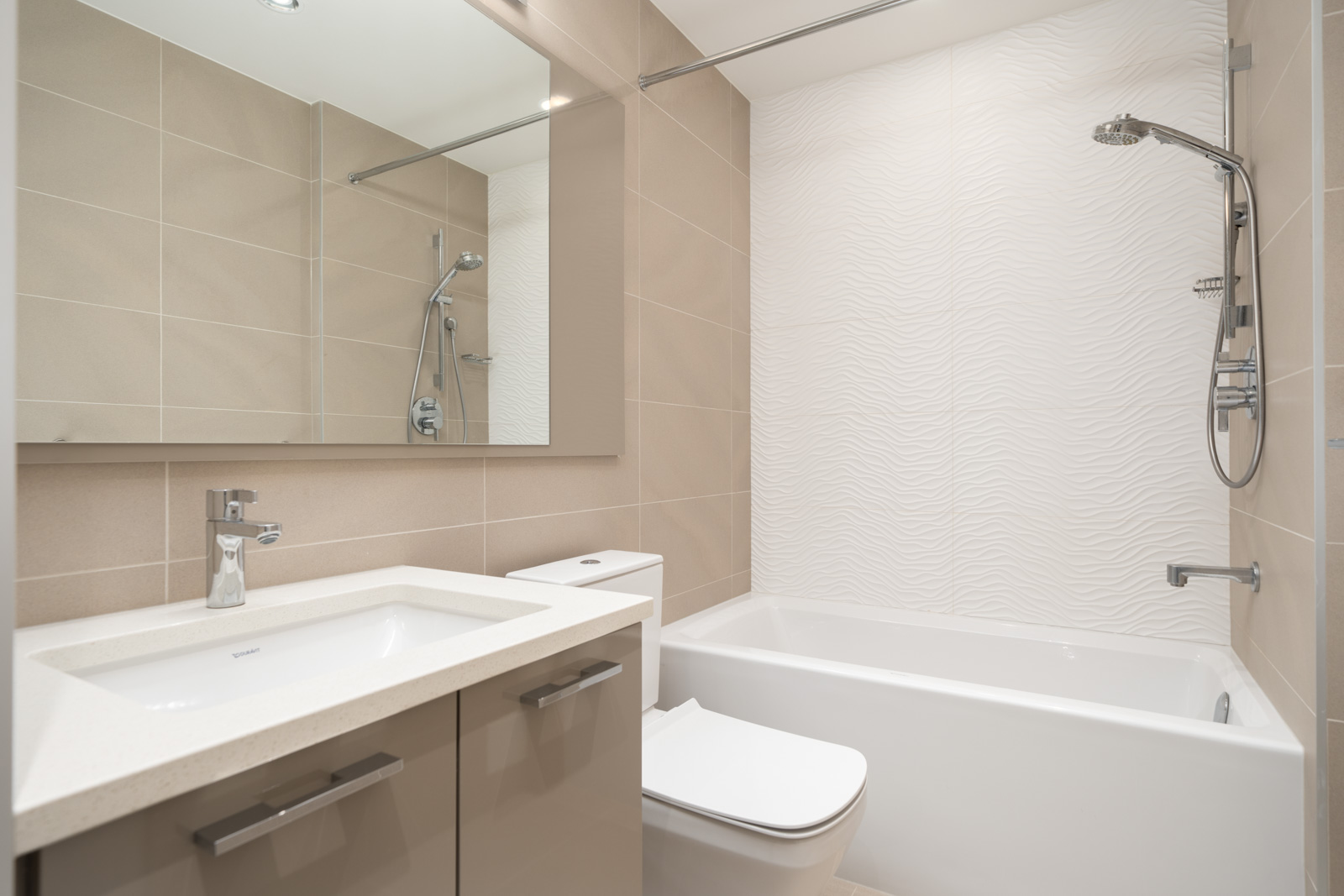 Modern bathroom with a large mirror, sink, toilet, and bathtub with a wall-mounted showerhead; beige tiles and white textured wall panel.