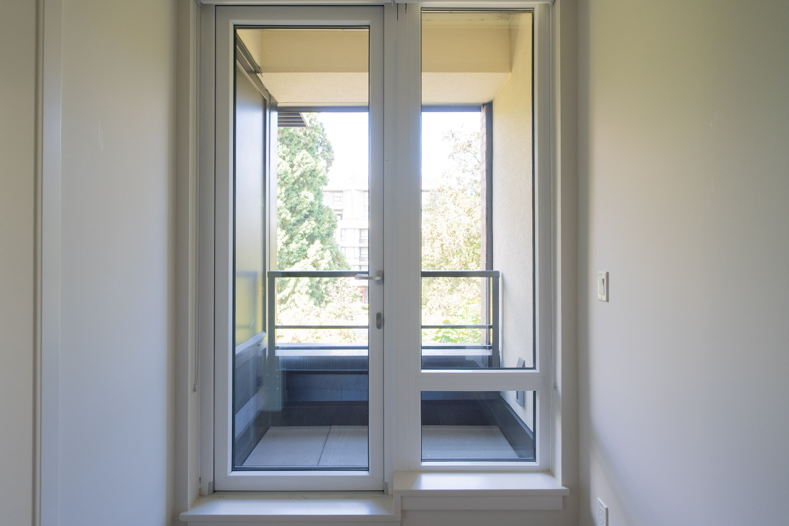 Glass door leading to a small, covered balcony with a railing and outdoor view; the scene is well-lit by natural light.