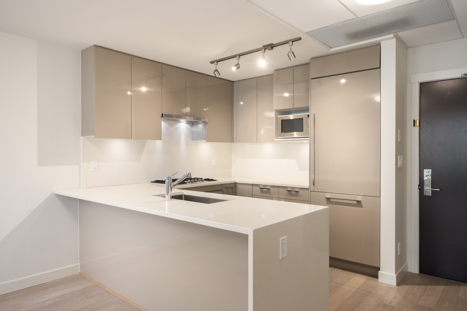 Modern kitchen with beige cabinets, built-in appliances, a white countertop peninsula, and overhead track lighting.