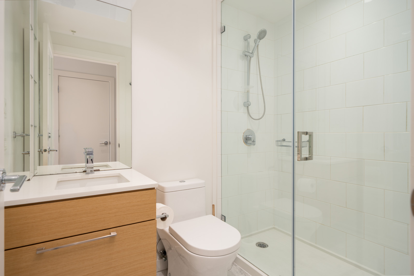 Modern bathroom with a glass-enclosed shower, white toilet, and wood vanity with a sink and faucet, all in a clean, minimal design.
