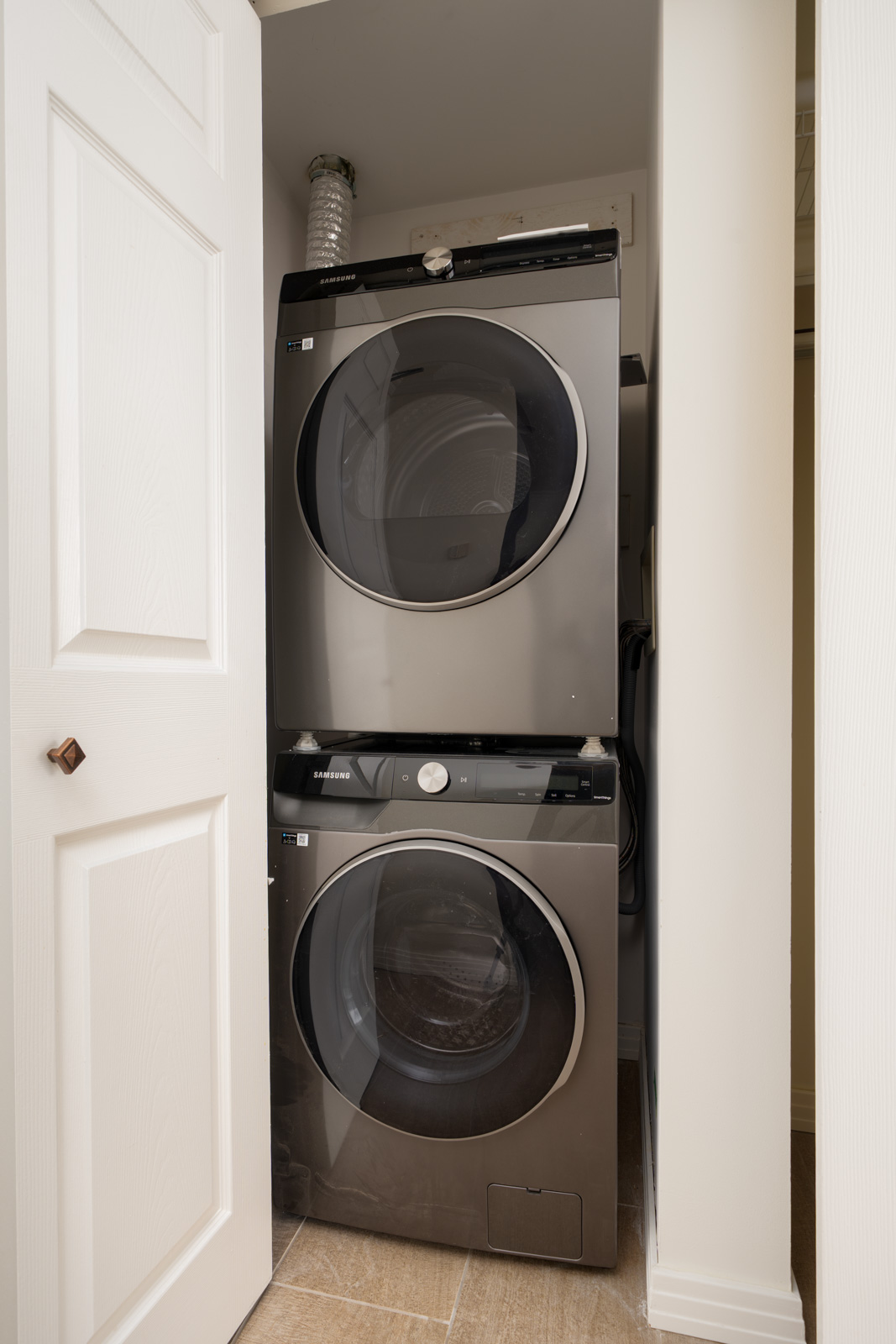 Stacked washer and dryer in a compact laundry closet with white doors and light tile floors at 189 Davie St, Vancouver.