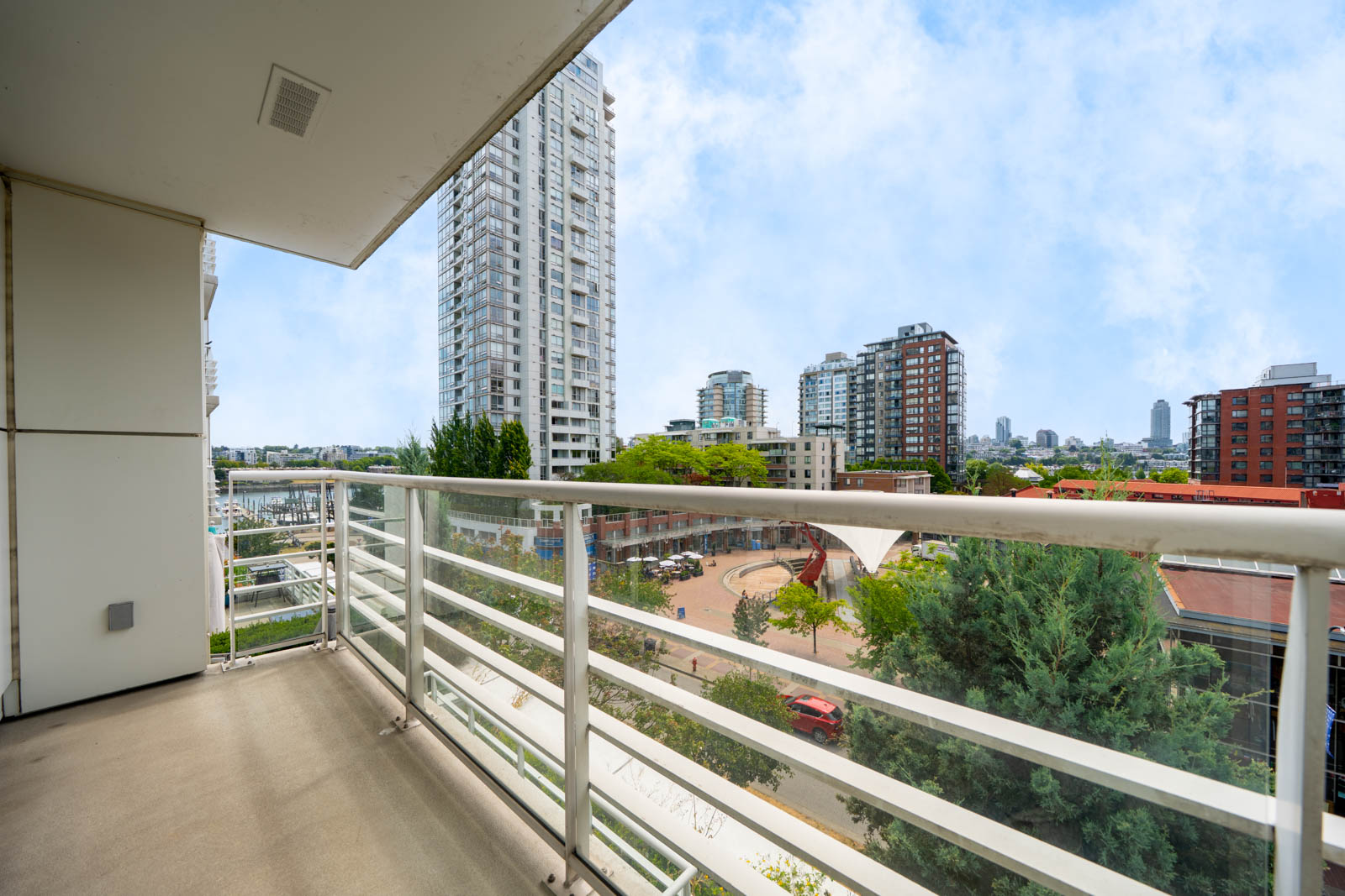 Sixth-floor balcony view at 189 Davie St, Vancouver: nearby apartments, public square with trees, and clear urban sky.