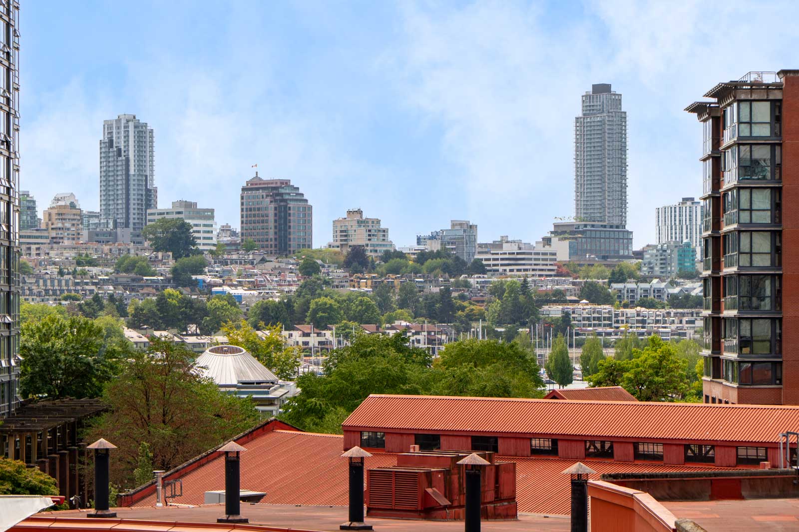 Vancouver cityscape with 189 Davie St, mid- and high-rises, red-roofed buildings in front, trees, and blue sky.