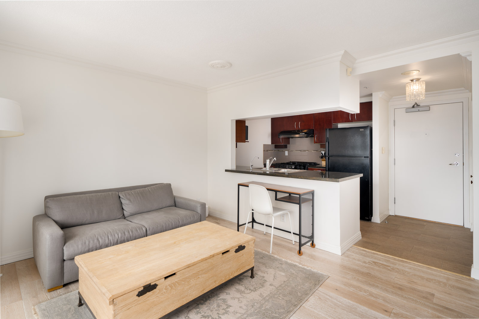 Modern studio apartment at 189 Davie St, Vancouver, with a gray sofa, wood coffee table, small kitchen, and light wood floors.