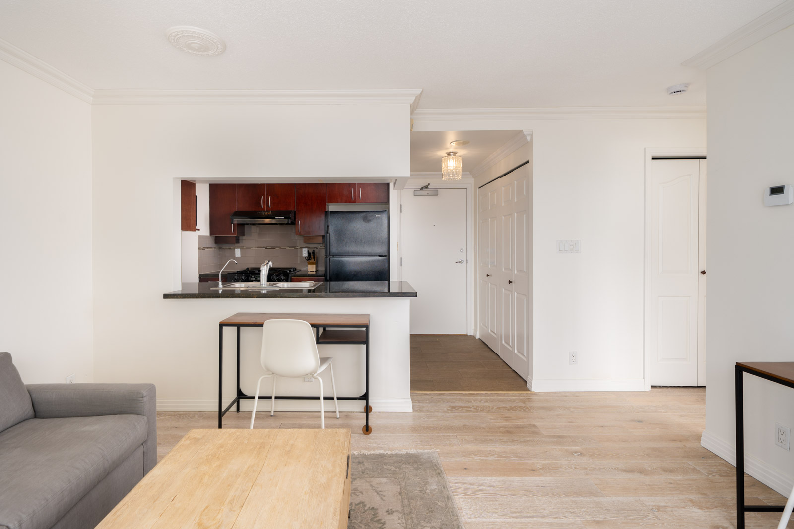 Open-plan living area on the 6th floor at 189 Davie St, Vancouver, with wood floors, gray sofa, and kitchen with dark cabinets.