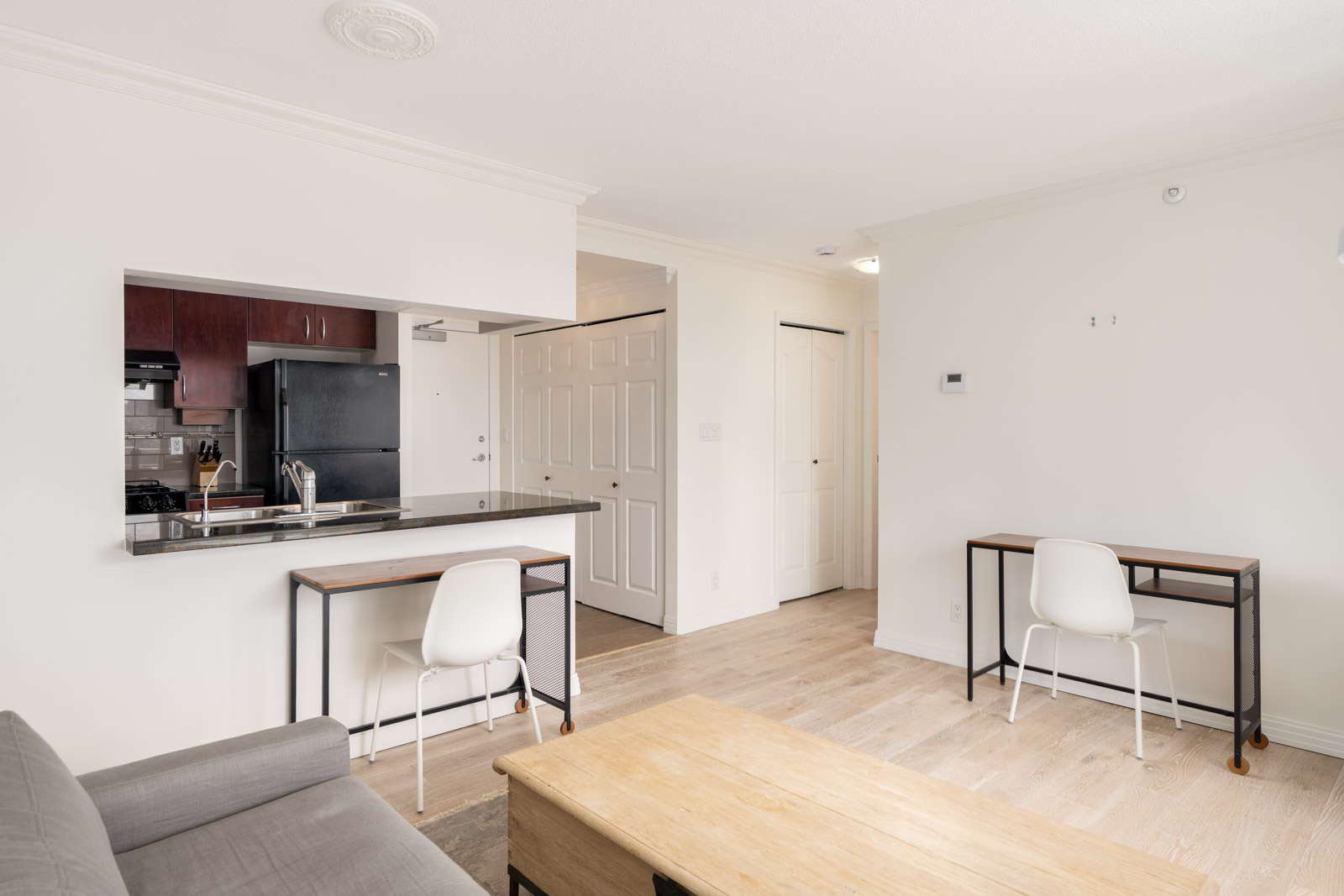 Bright Vancouver apartment at 189 Davie St with a small kitchen, black appliances, breakfast bar, two desks, gray sofa, and wood floors.