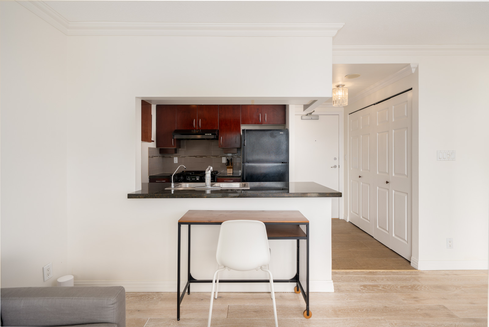 A small Vancouver kitchen with dark cabinets and black appliances is seen through a pass-through, with a desk and hallway in front.