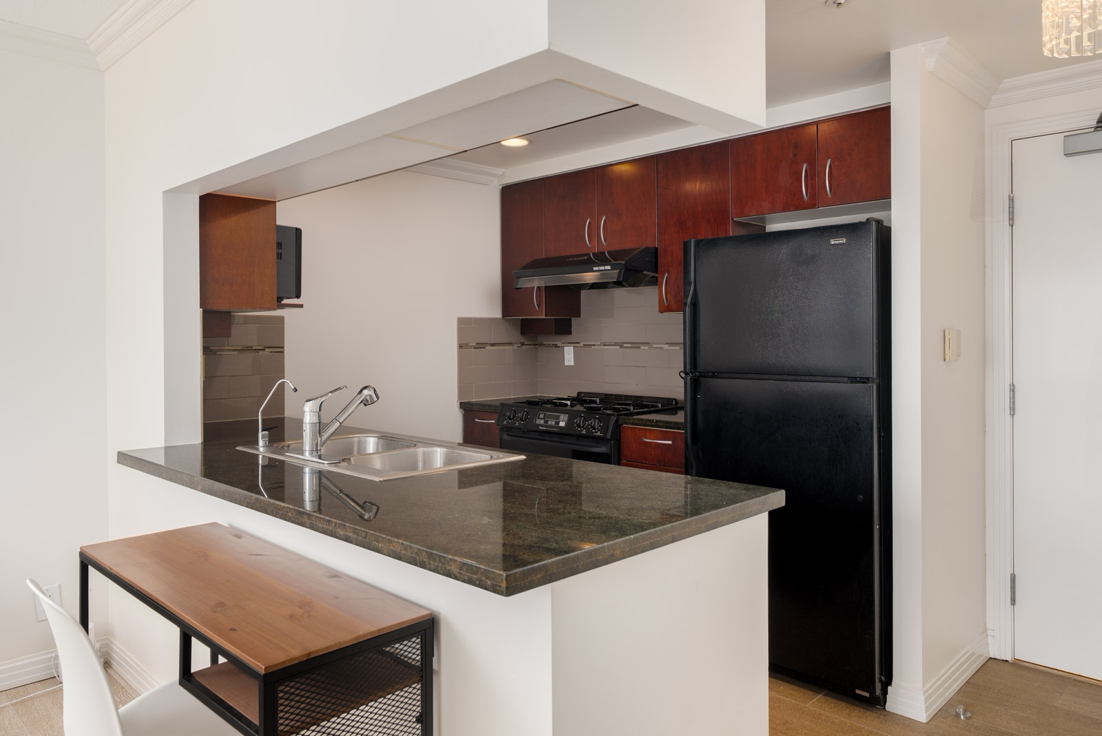 Modern 6th floor kitchen at 189 Davie St, Vancouver with dark counters, black fridge, gas stove, wood cabinets, and small dining area.
