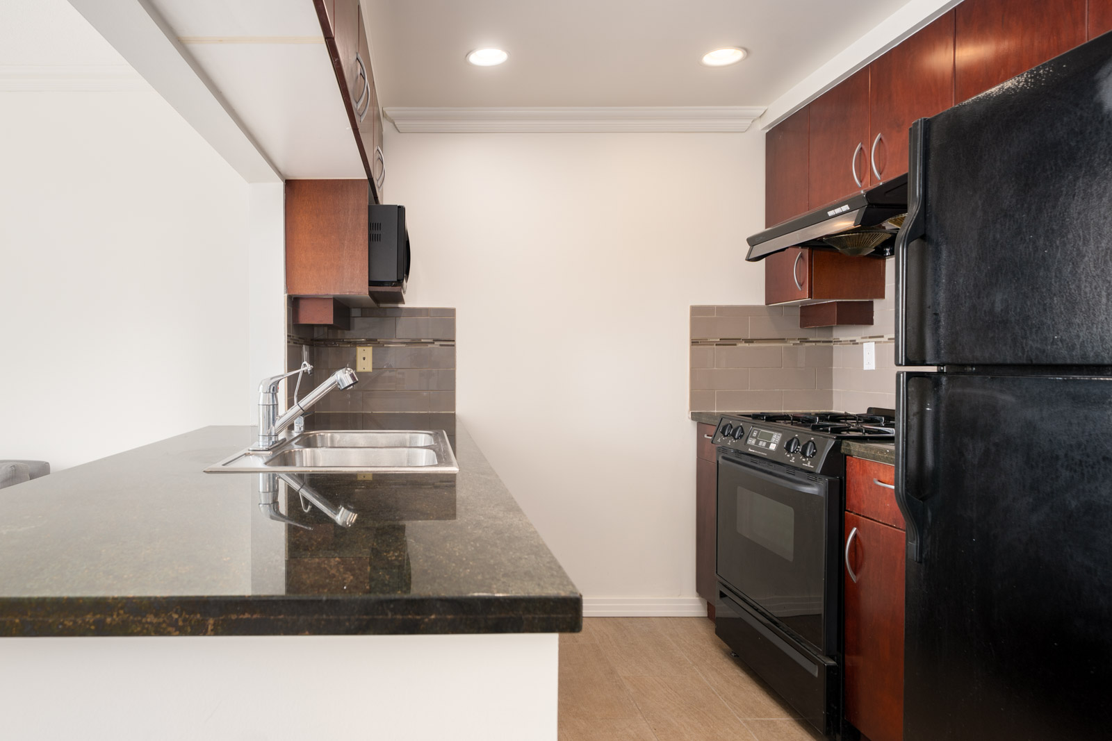 Modern kitchen at 189 Davie St, Vancouver with black appliances, dark counters, brown cabinets, double sink, and beige tile floor.