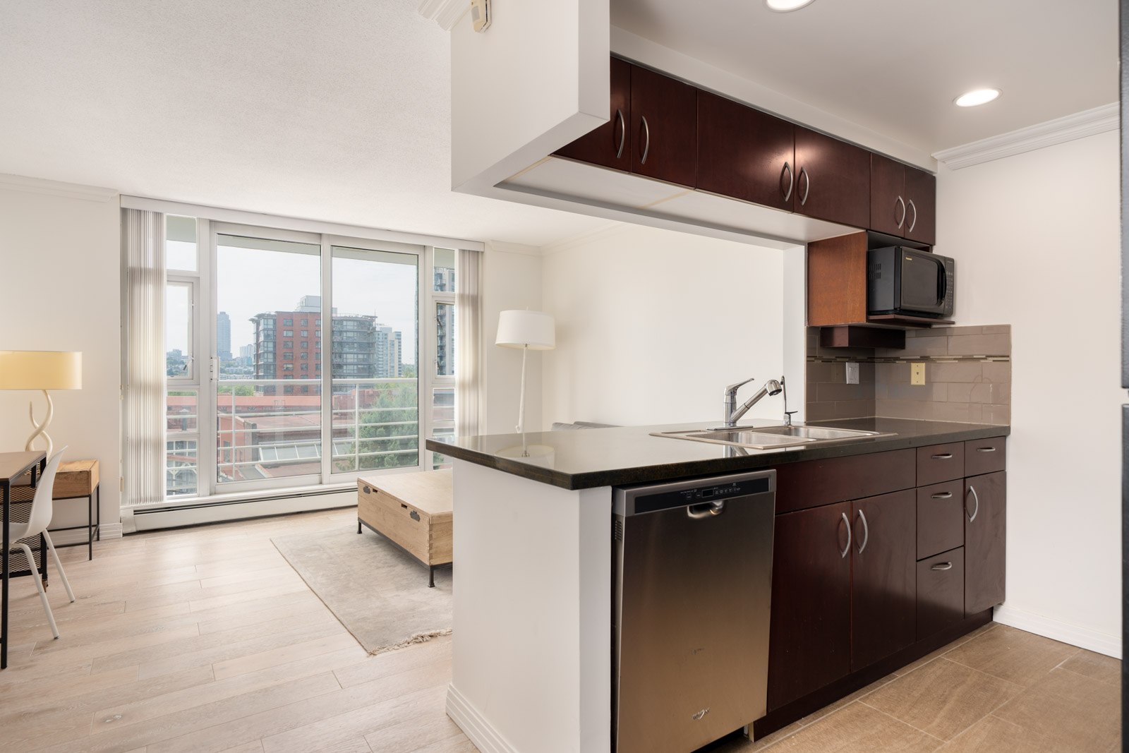 Apartment interior at 189 Davie St, Vancouver, with open kitchen, stainless appliances, large windows, and city views.