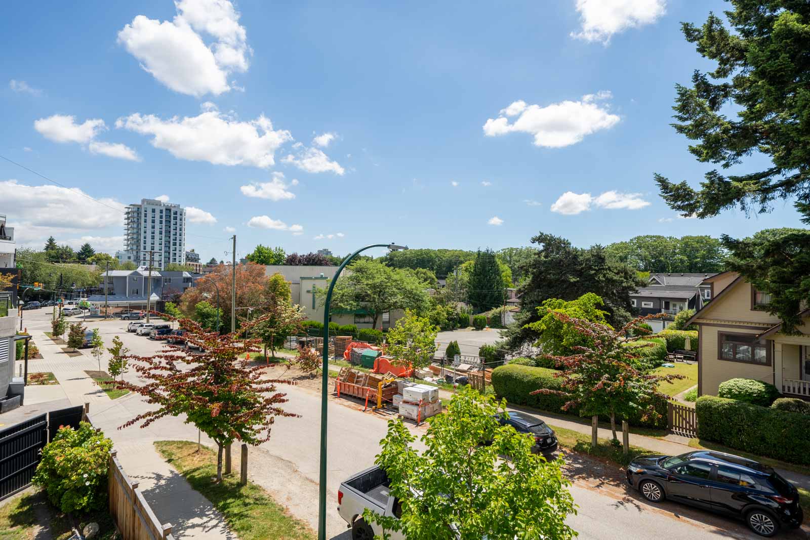E 19th Ave near St Catherines St, Vancouver: parked cars, houses, trees, construction materials, and a tall building in back.