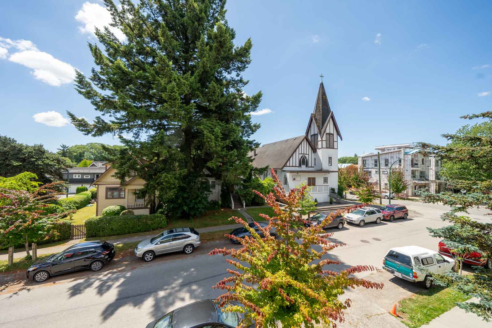 Street view on E 19th Ave near St Catherines St, Vancouver: parked cars, tall tree, white church steeple, houses, construction.