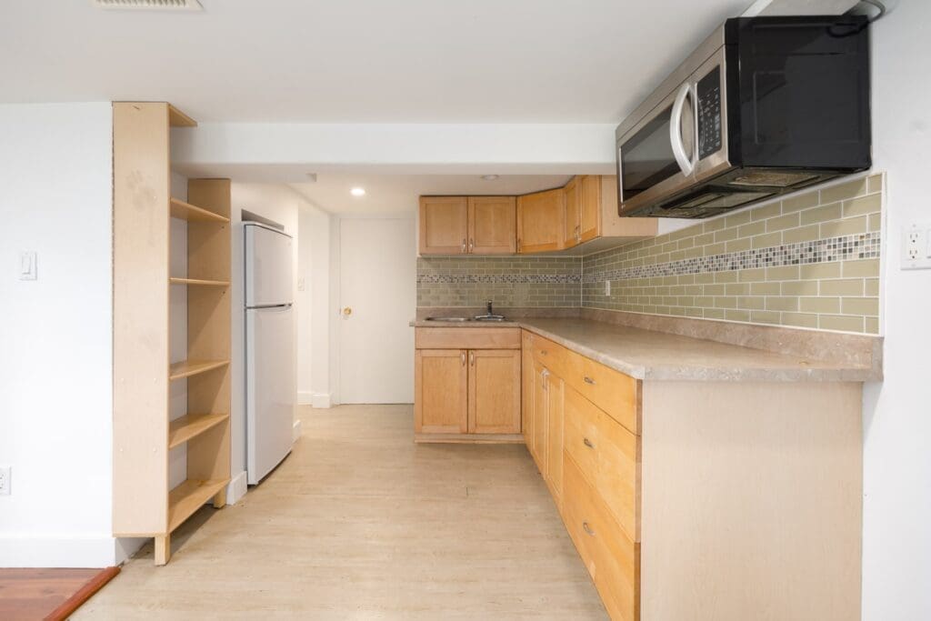 Small kitchen on E 19th Ave, Vancouver with wooden cabinets, beige counters, open shelves, green tile backsplash, and white walls.