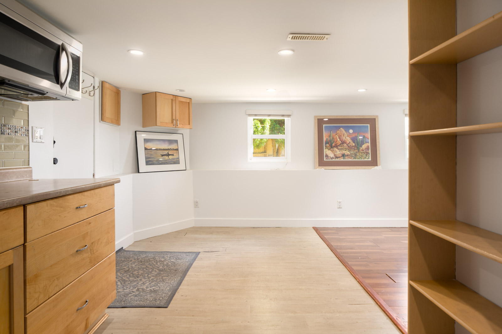 Room with light wood cabinets, microwave, shelving, mixed flooring, window and artwork; recessed lights. Near St Catherines St, Vancouver.