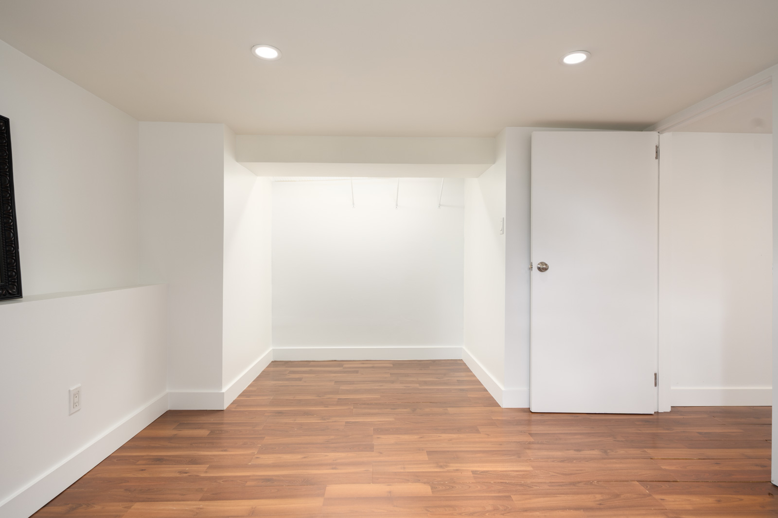 Bright white room with recessed lights, wood flooring, open door on right, and back alcove; in Vancouver near St Catherines St and E 19th Ave.