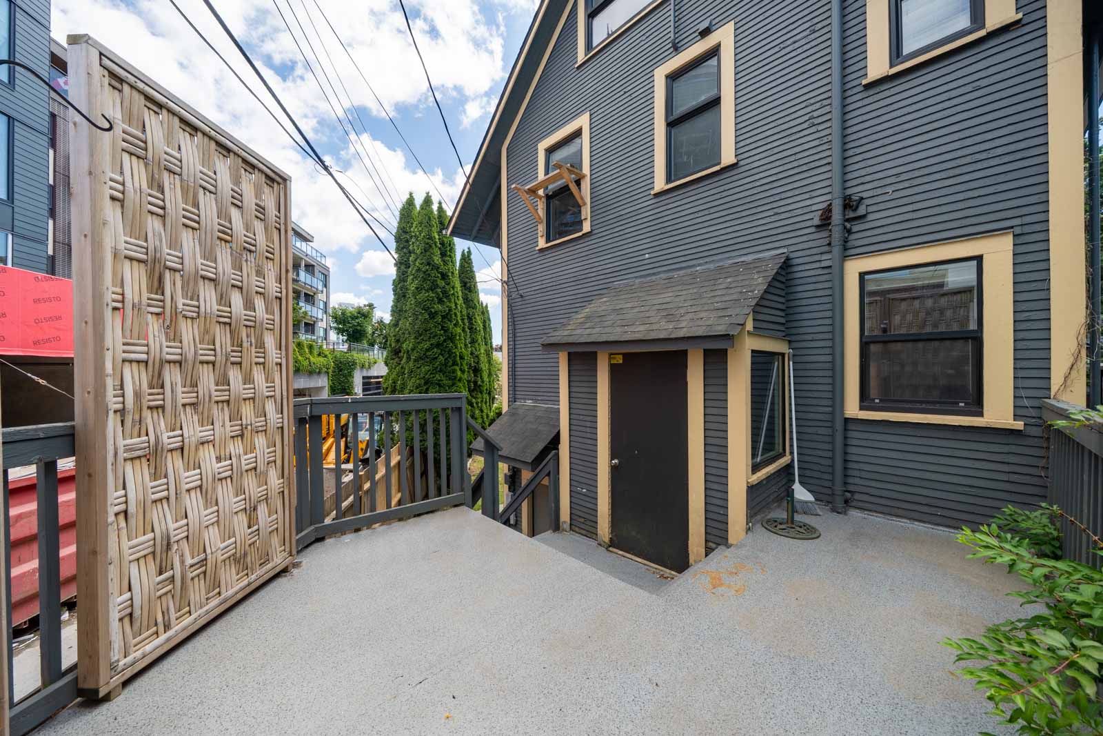 Gray house with beige trim, small entryway, deck, and lattice screen amid greenery on a sunny day in Vancouver.
