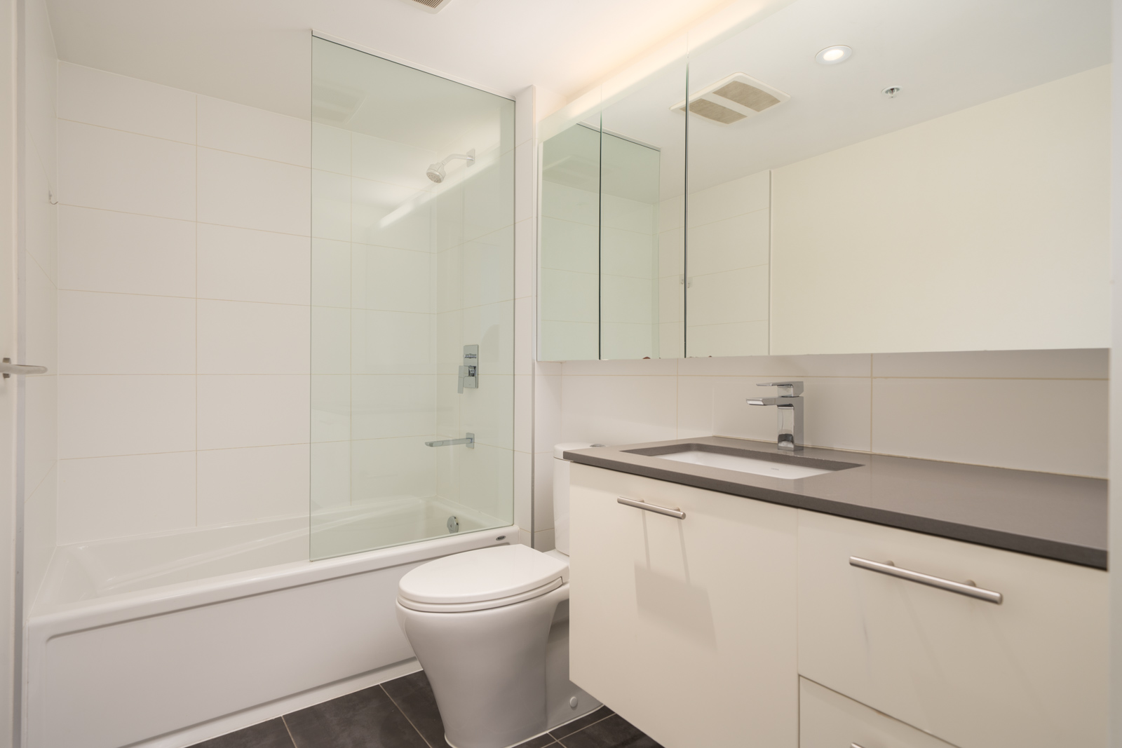 Contemporary bathroom featuring a bathtub, glass shower, white vanity with dark countertop, wall mirror, and tiled floor.