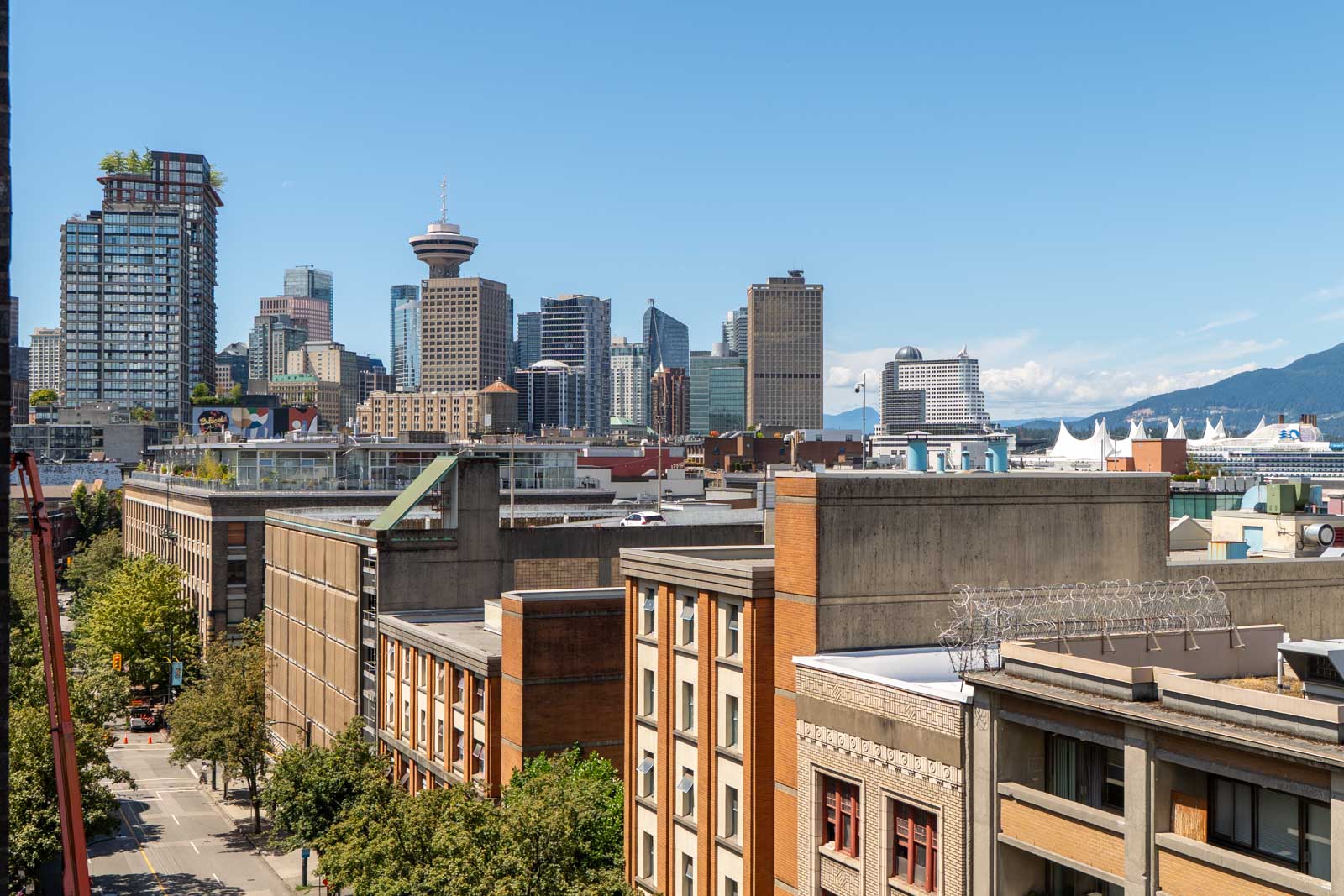 Downtown skyline with glass high-rises, older brick buildings in front, and distant mountains under a clear blue sky.