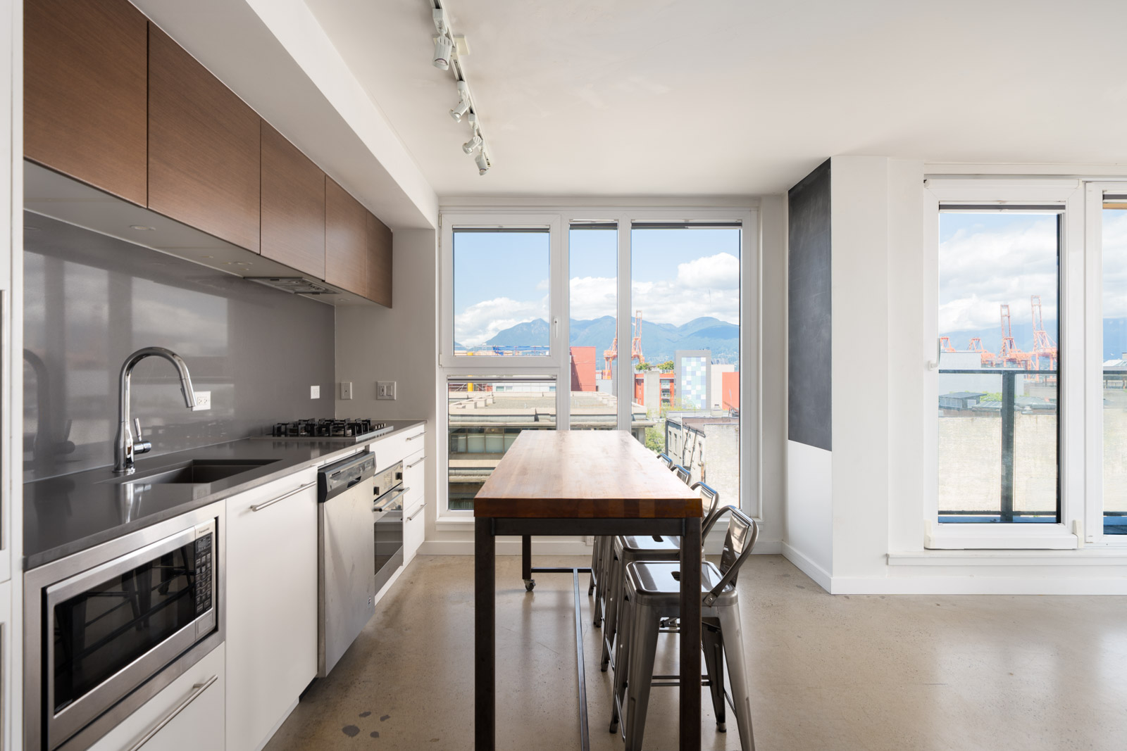 Modern kitchen with white cabinets, stainless appliances, wood dining table, metal chairs, large windows, and mountain views.