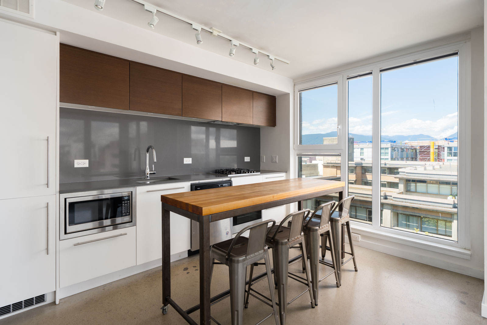 Modern kitchen with white cabinets, wood island, metal stools, built-in appliances, large window, city and mountain views.