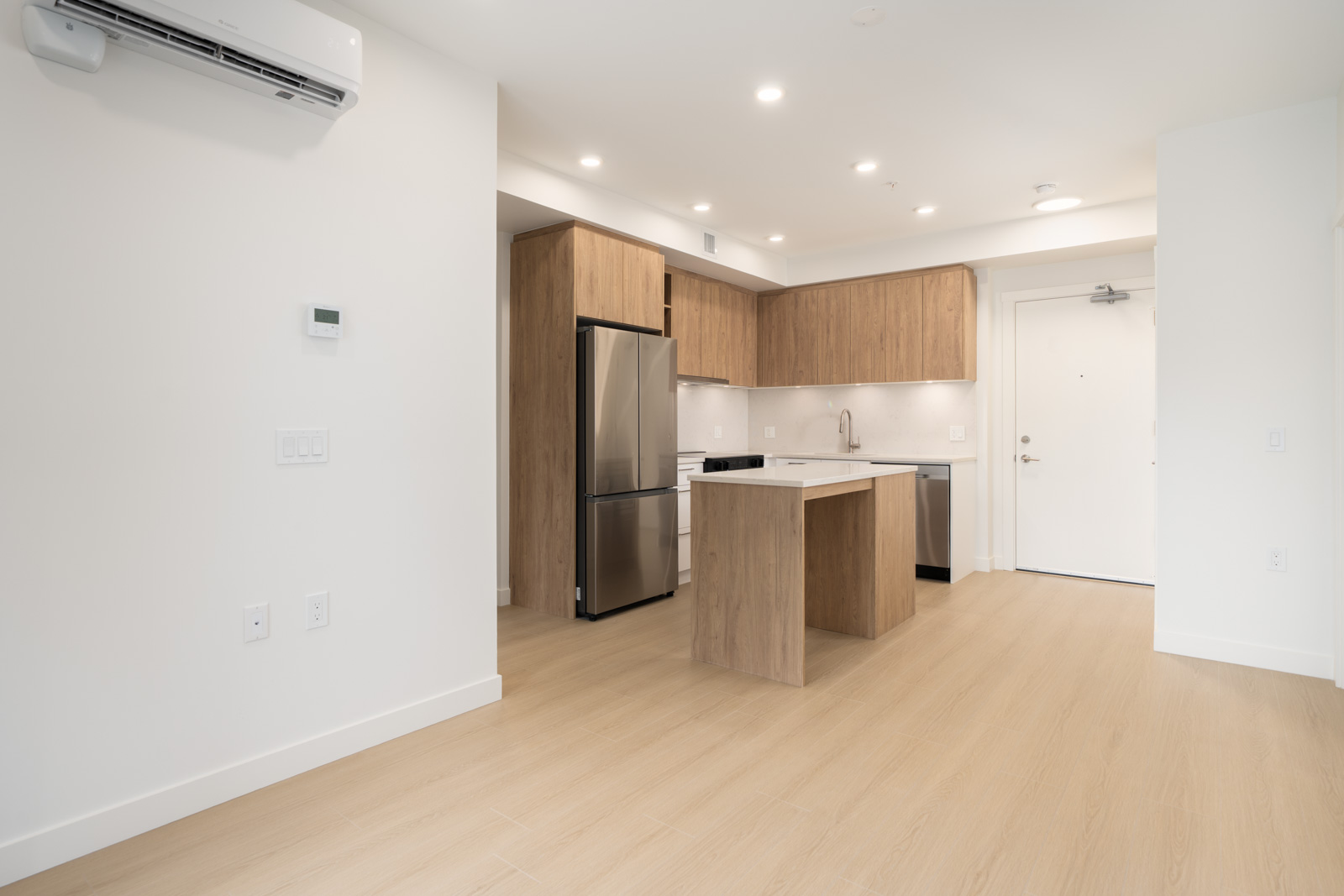 Bright open-concept kitchen with wood cabinets, stainless steel appliances, light wood floors, and white walls.