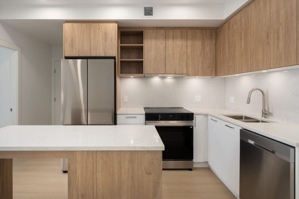 Contemporary kitchen with wood cabinets, white counters, stainless appliances, island, and under-cabinet lighting.