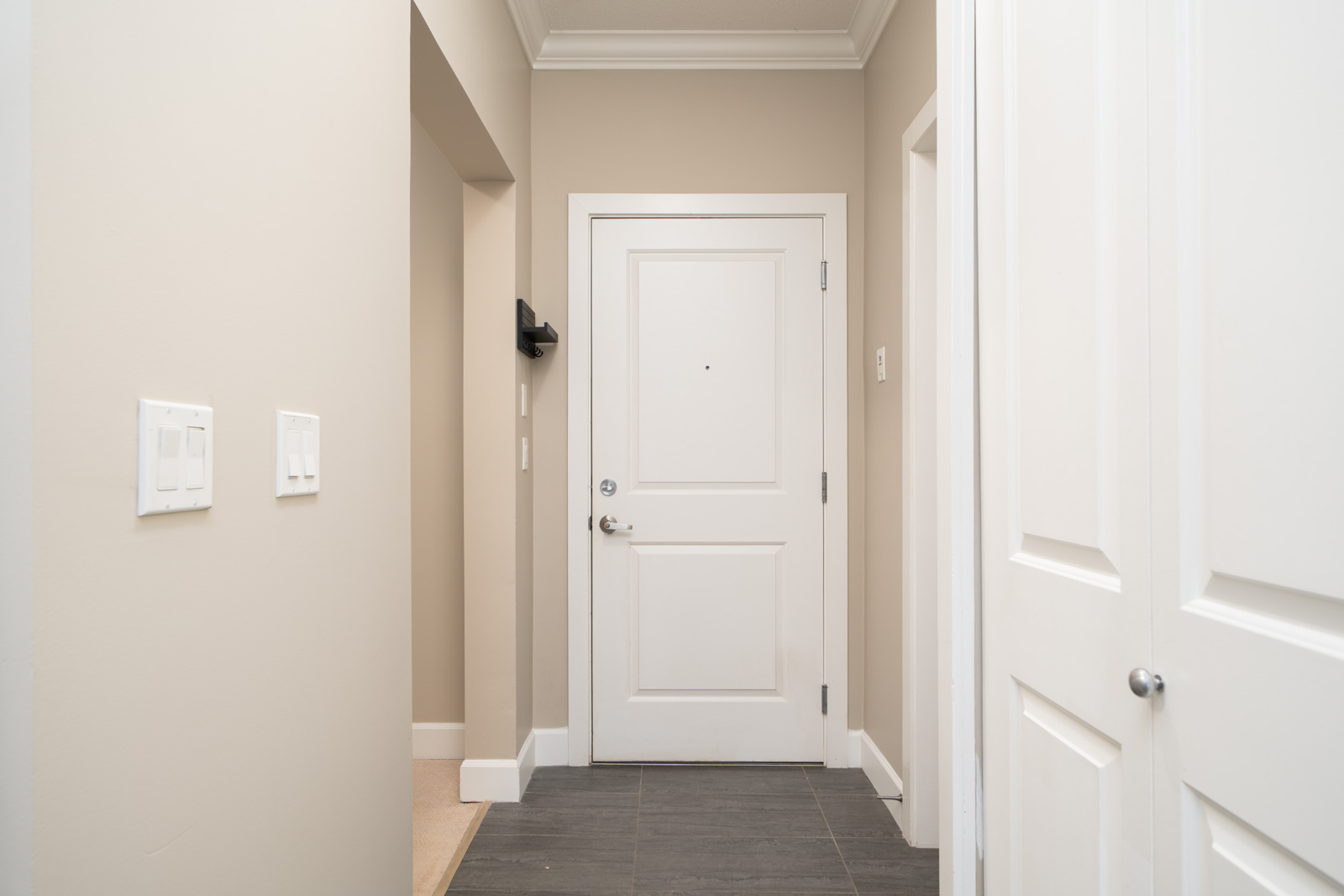 A white front door with a silver handle in a beige entryway along Fraser Highway, Surrey; dark tile floor, doors to the right.
