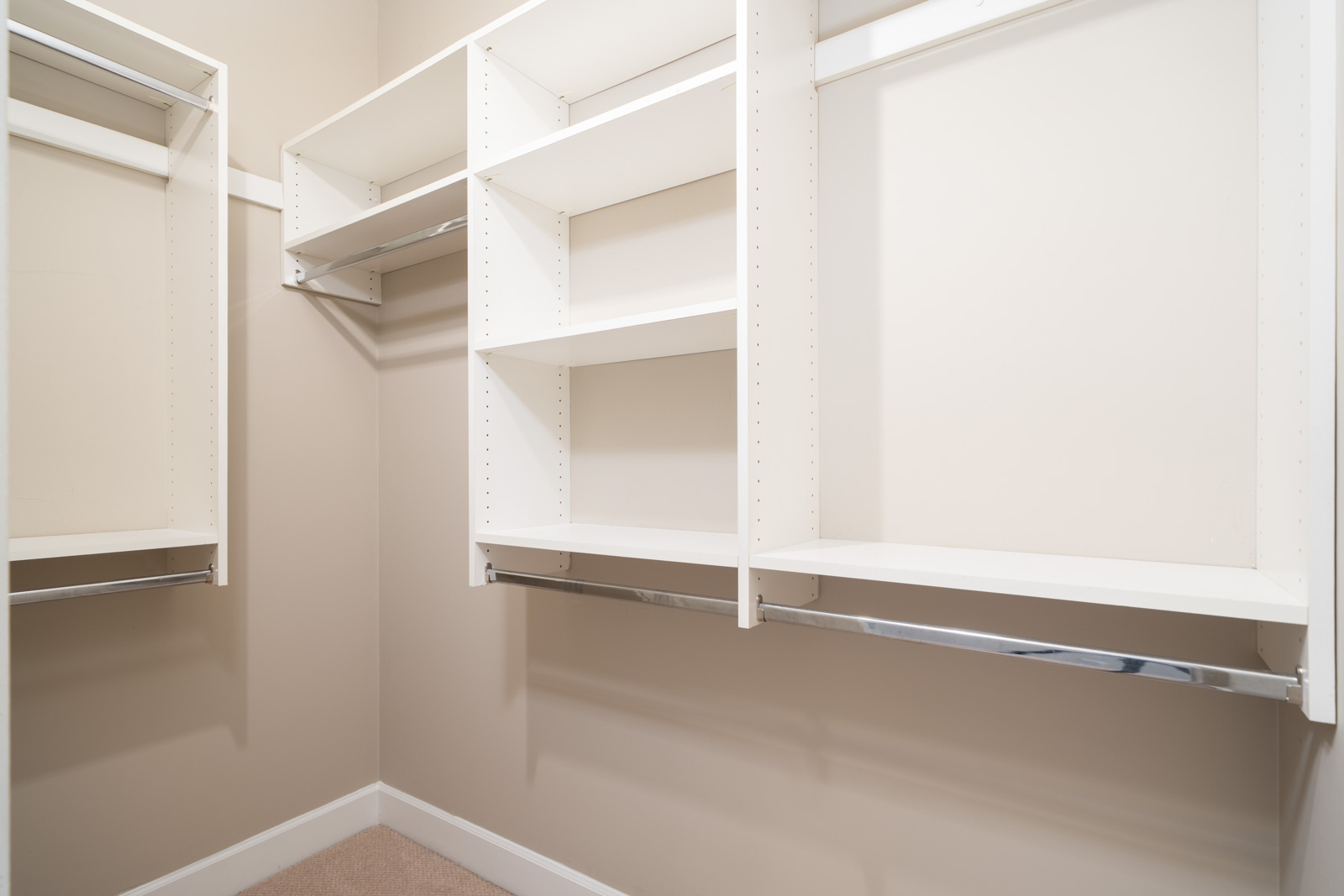 Walk-in closet with white shelves, hanging rods, beige walls, and light carpet in Surrey, minutes from Fraser Highway.