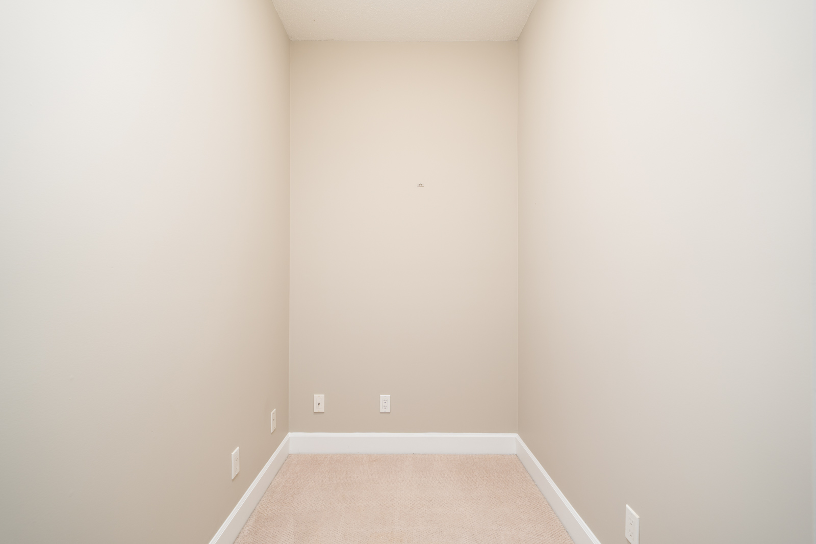 Empty room with beige carpet, cream walls, white baseboards, and multiple outlets along the back wall in Surrey off Fraser Highway.