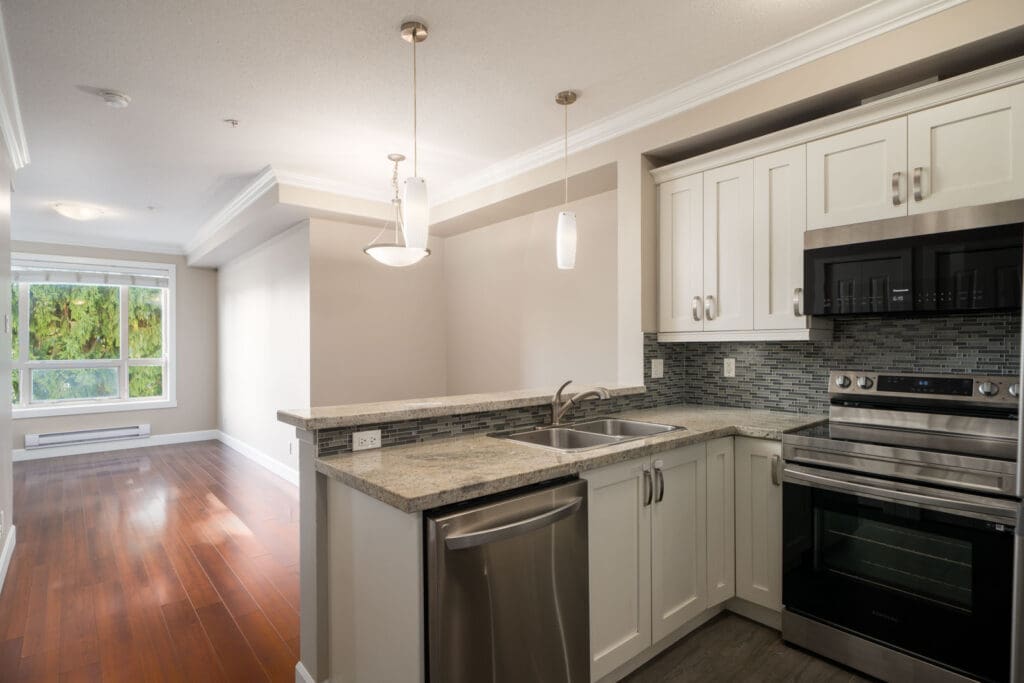 Modern kitchen with white cabinets, stainless appliances, double sink, and breakfast bar in Surrey; next to bright living area.