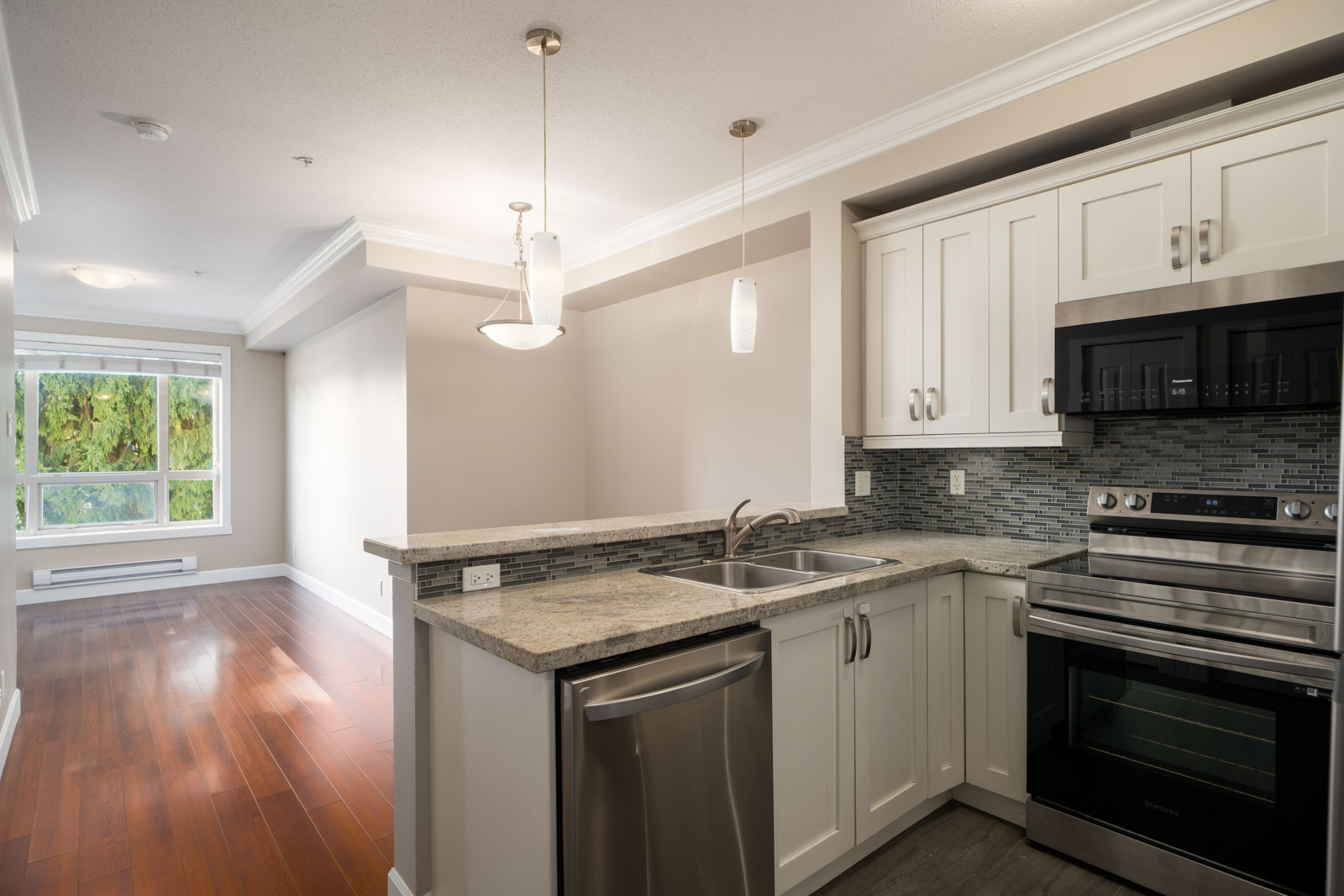 Modern kitchen with white cabinets, stainless appliances, double sink, and breakfast bar in Surrey; next to bright living area.
