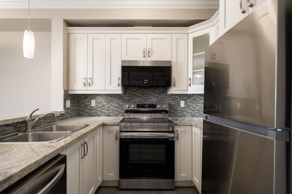 Modern kitchen in Surrey near Fraser Highway with stainless appliances, white cabinets, dual sink, tile backsplash, and granite counters.