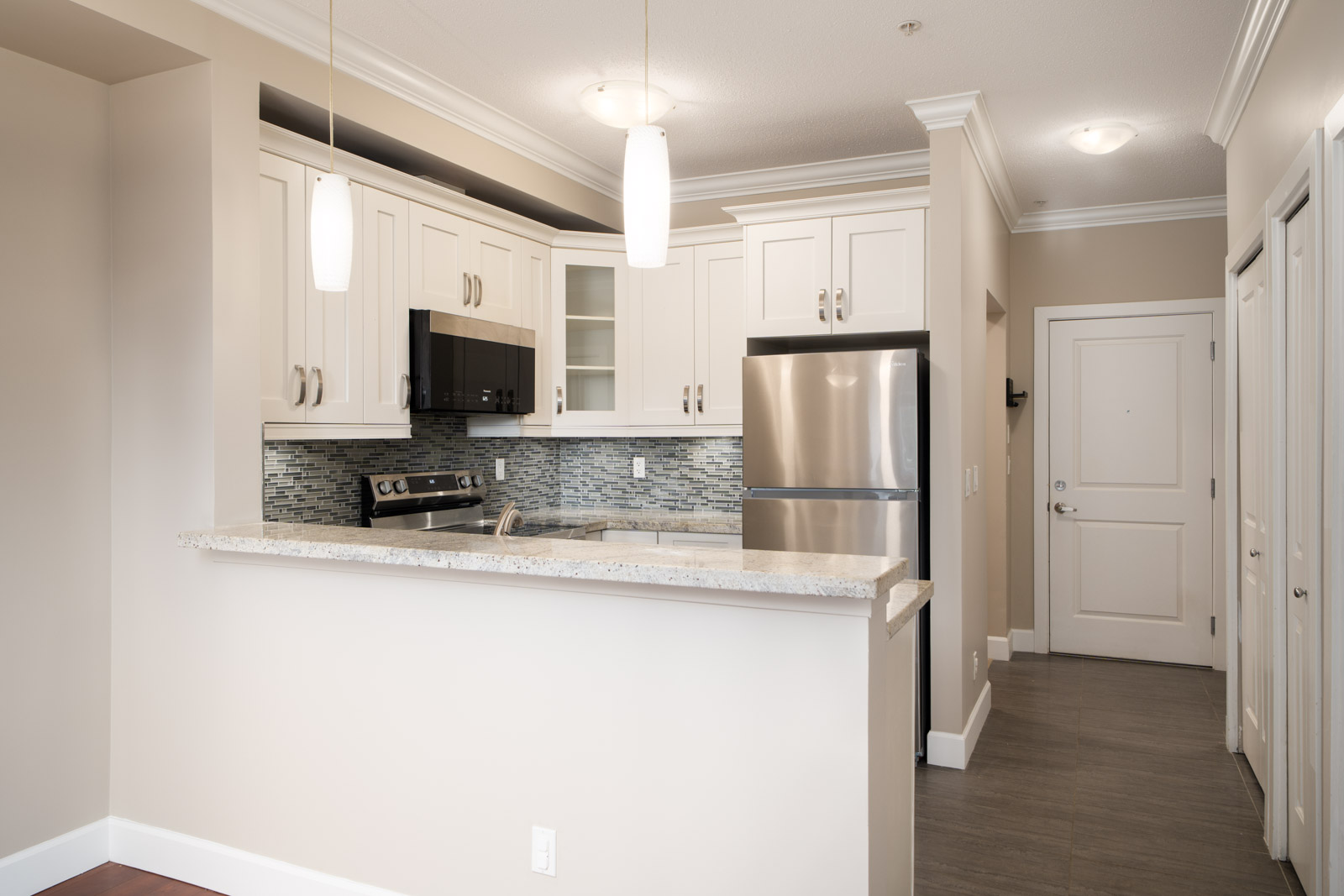 Modern kitchen with white cabinets, stainless appliances, mosaic tile backsplash, breakfast bar, and view of hallway in Surrey.