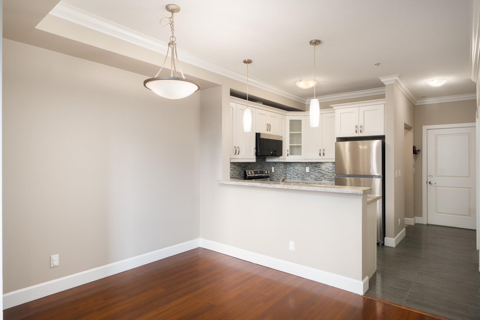 Modern kitchen in Surrey near Fraser Highway with white cabinets, stainless steel appliances, wood floors, and pendant lights.