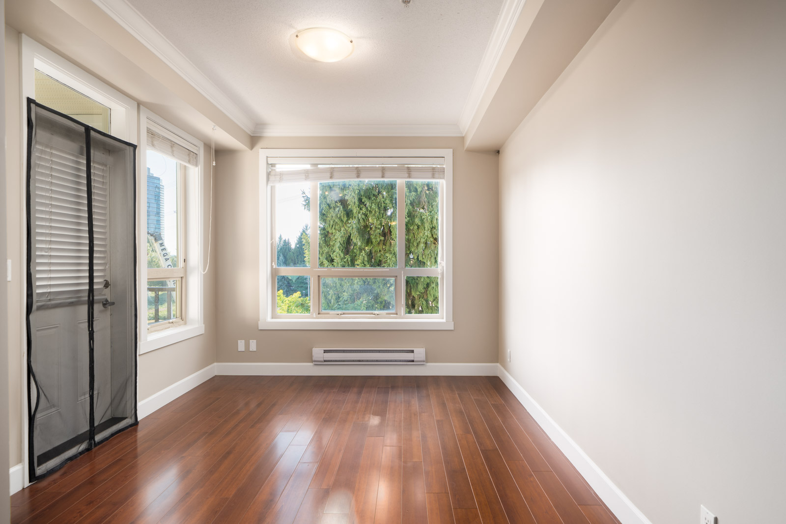 Empty room with hardwood floors, beige walls, large windows with blinds, screen door to outside; Surrey and Fraser Hwy in view.