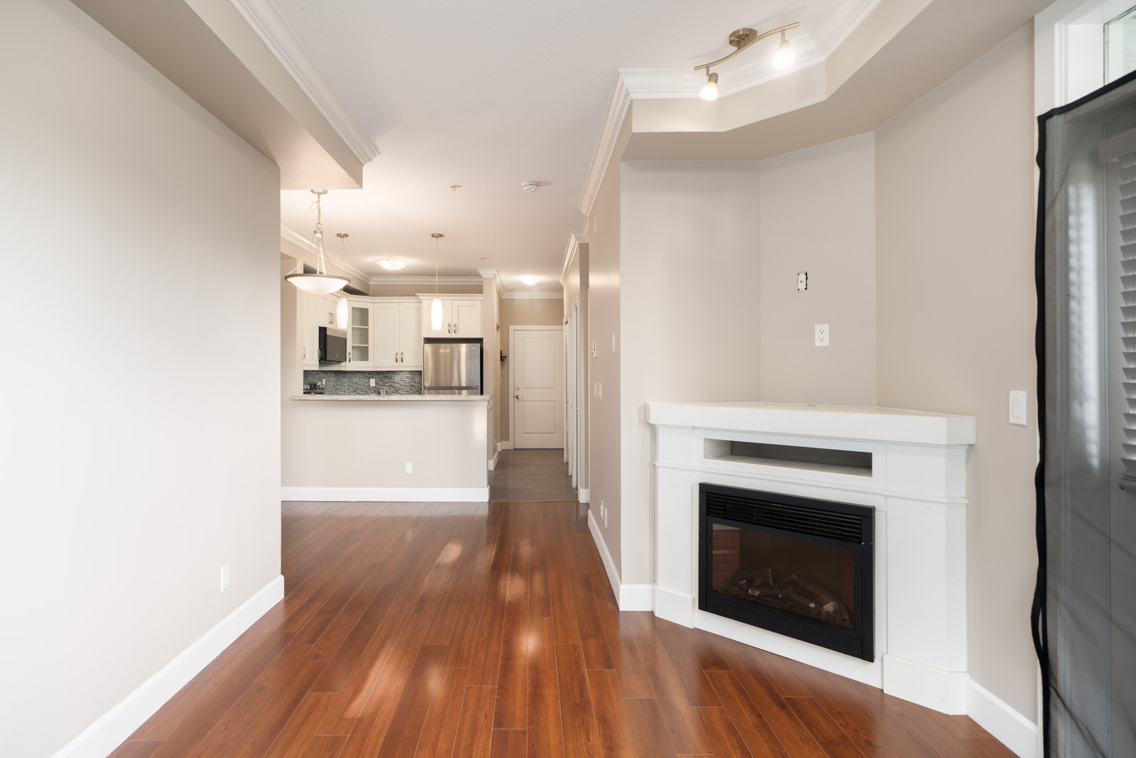 Unfurnished Surrey apartment with hardwood floors, fireplace, neutral walls, and kitchen with stainless steel appliances.