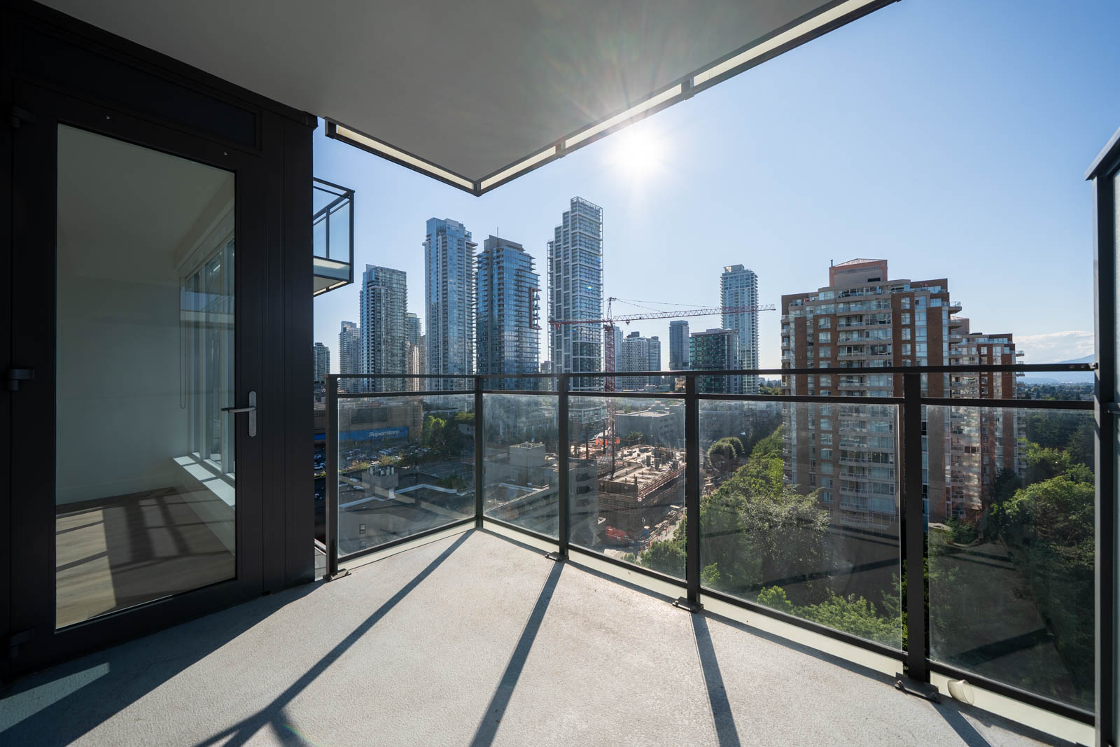 View from a modern apartment balcony overlooking a cityscape with high-rise buildings, construction site, and clear sky with the sun shining.