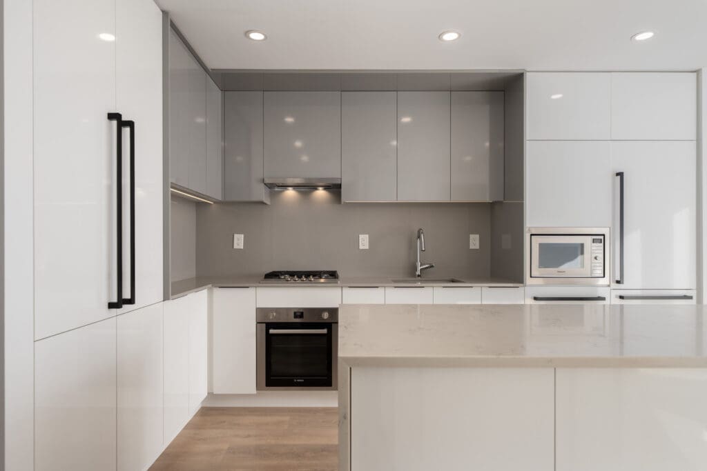 Modern kitchen with glossy white cabinets, gray upper cupboards, built-in oven, cooktop, microwave, sink, and a large island under recessed lighting.