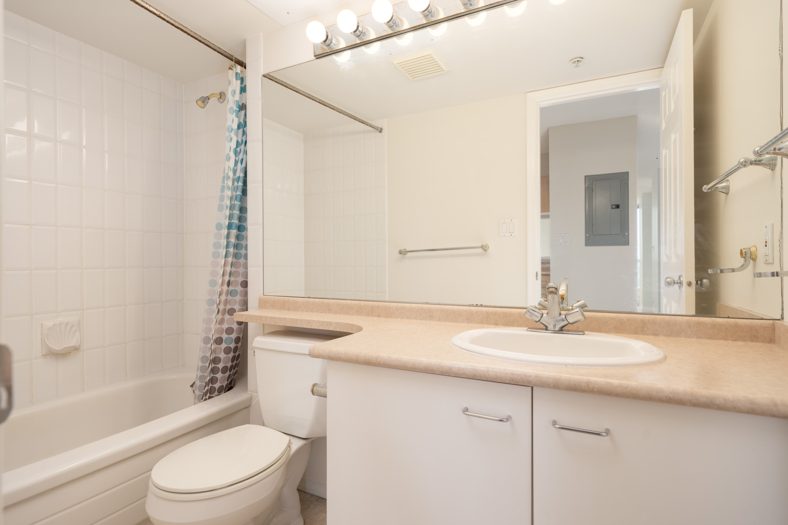 A tidy bathroom on Heffley Crescent’s 1st floor in Coquitlam with white sink, toilet, bathtub, shower curtain, mirror, and overhead lights.