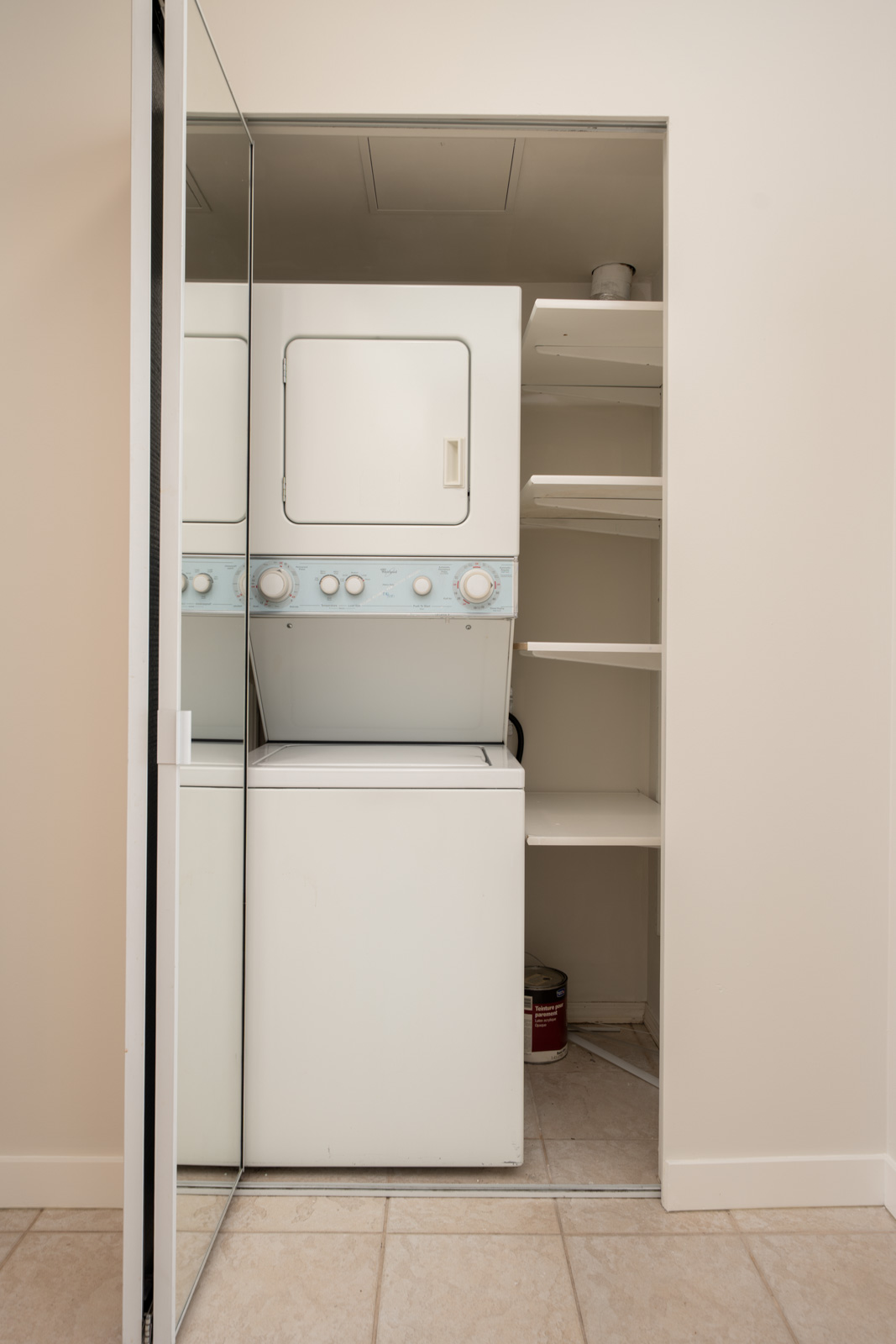 Partially open mirrored sliding closet door reveals stacked washer and dryer beside white shelves on the first floor in Coquitlam.