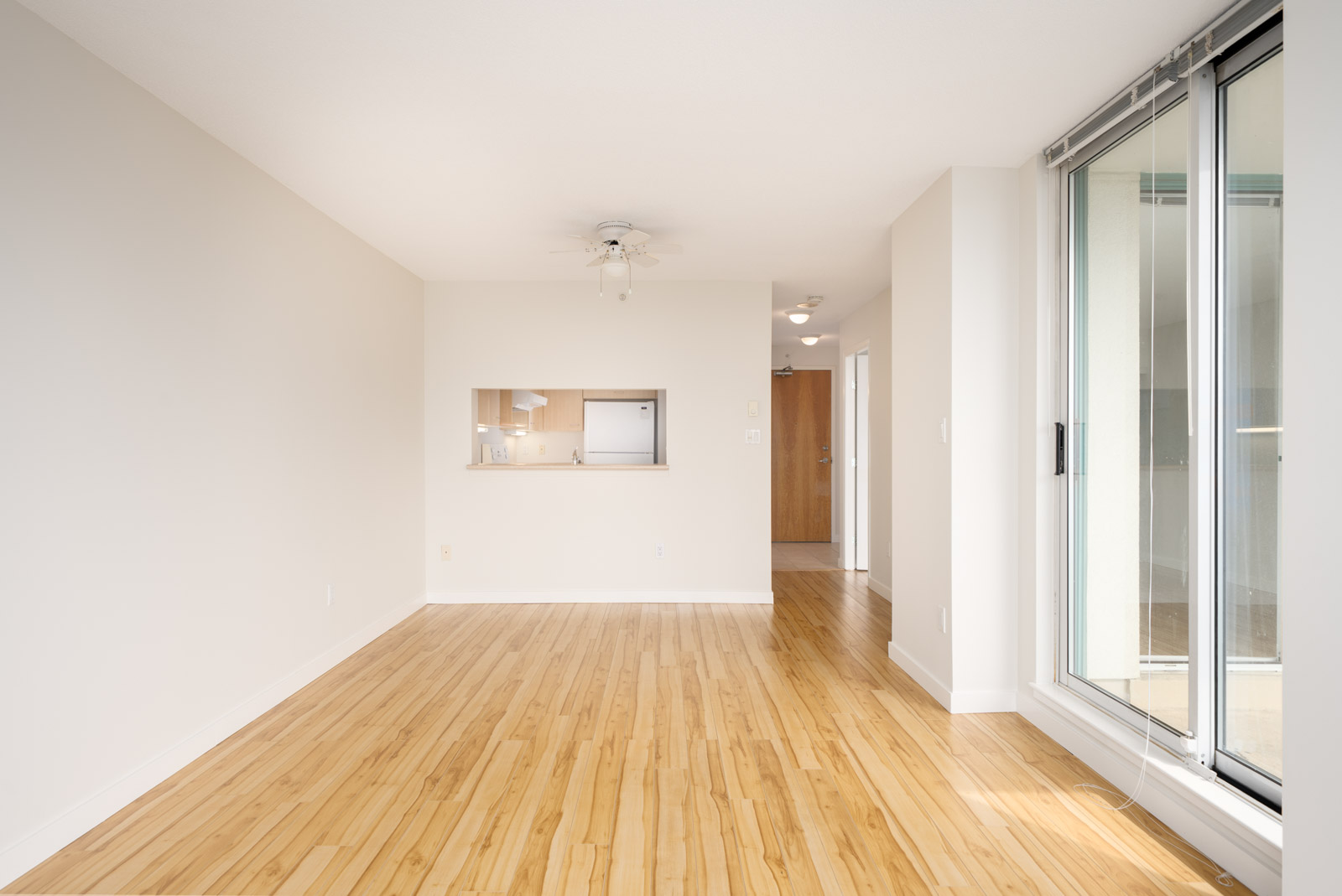 Empty 1st floor apartment room in Coquitlam with light wood floors, white walls, ceiling fan, and sliding doors to balcony.