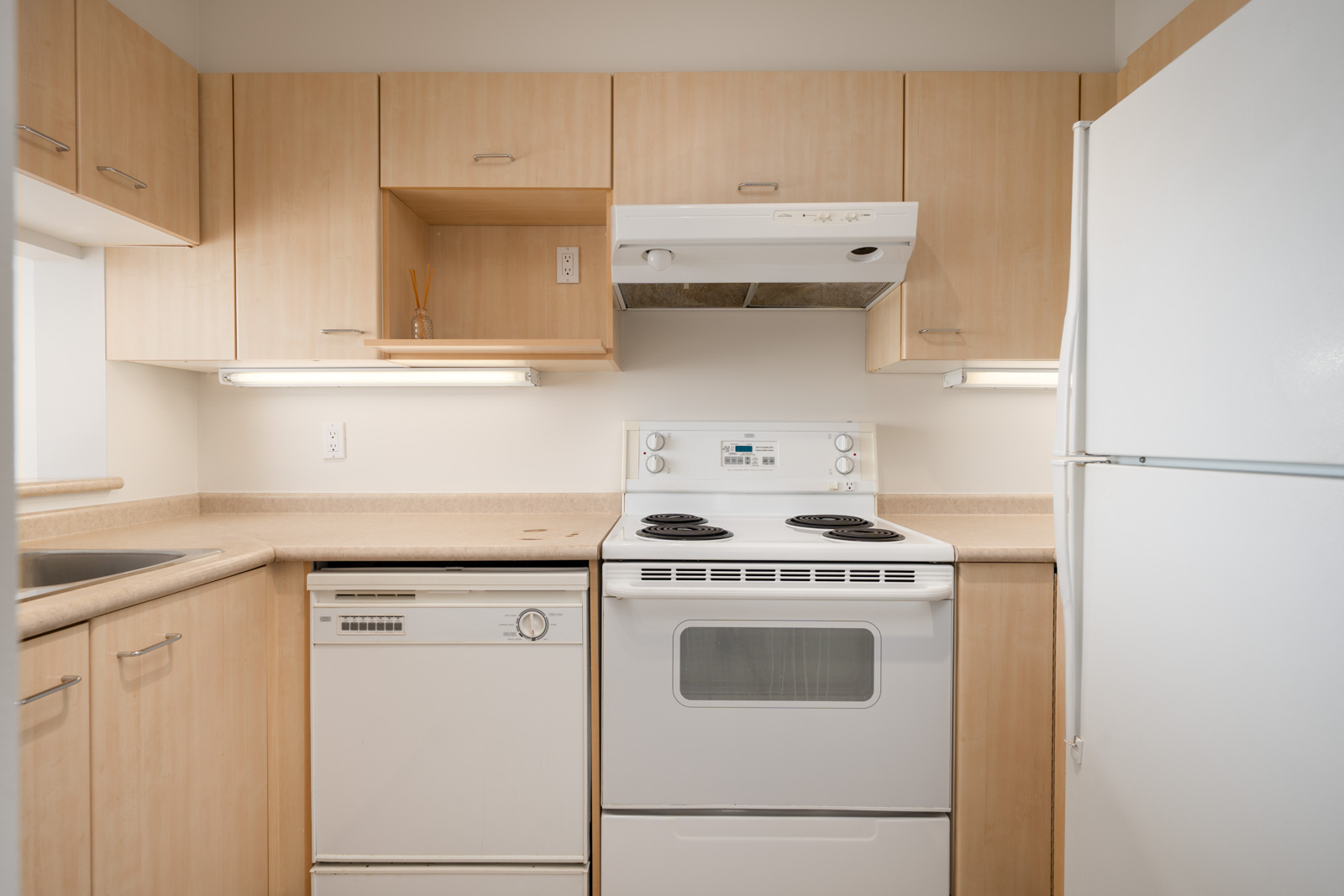 Small 1st floor kitchen with light wood cabinets, white appliances, beige counters, under-cabinet lights in Coquitlam near Heffley Crescent.