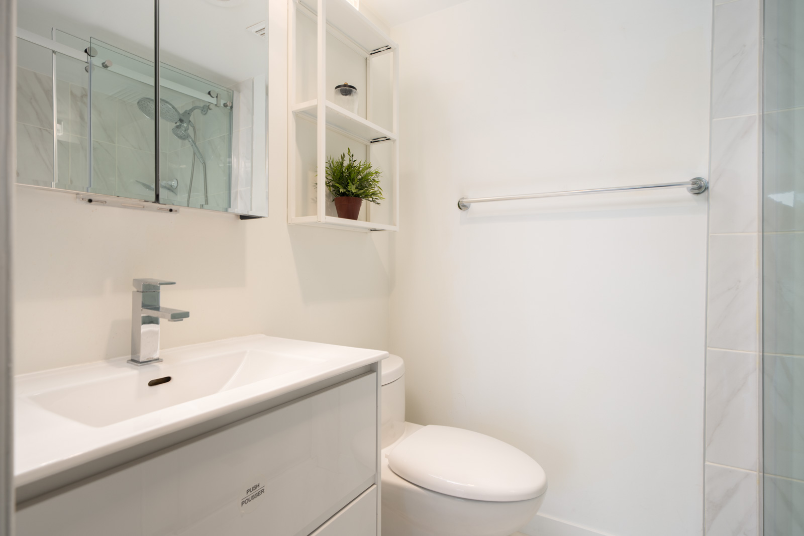 Modern bathroom with a wall-mounted sink, white cabinet, toilet, glass shower, towel bar, mirrored cabinet, and a small potted plant on a shelf.
