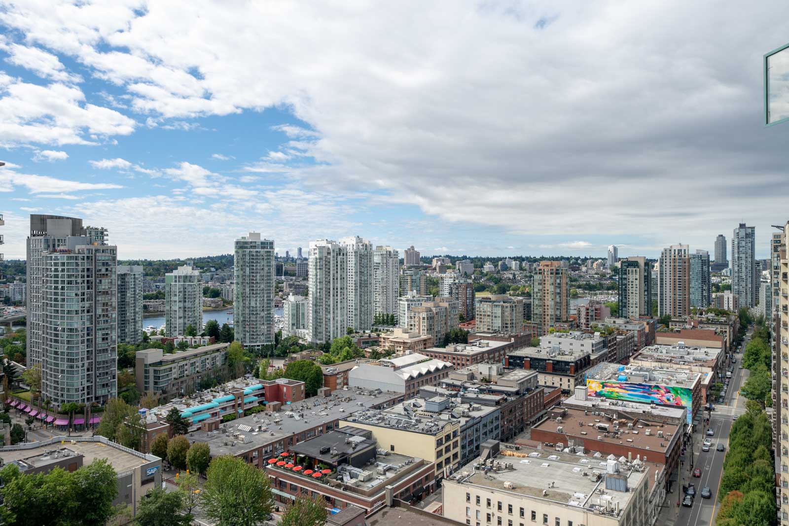 A cityscape shows high-rise buildings, mid-rise apartments, and a mix of commercial and residential structures under a partly cloudy sky.