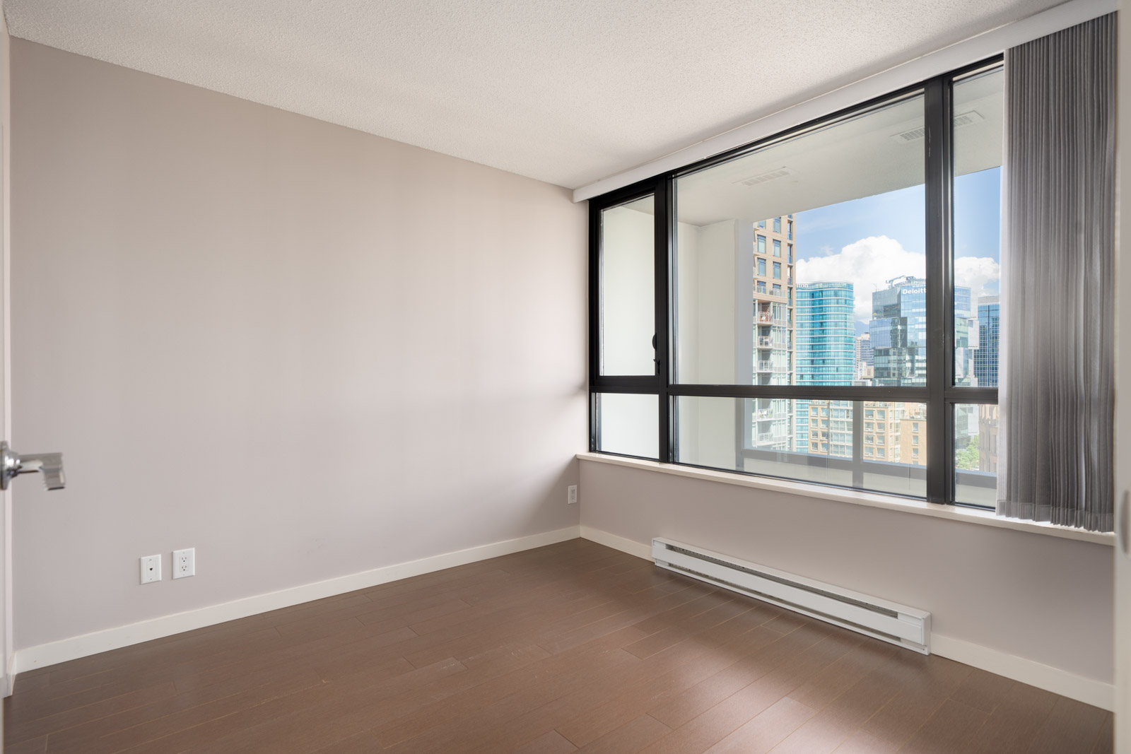 Unfurnished corner room with light brown walls and floor, large window with city view, and white baseboard heater at 909 Mainland St, Vancouver.